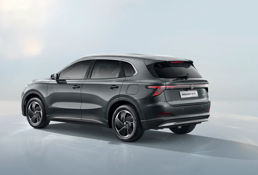 Nowy MGS5 EV - ile kosztuje? Nowoczesny, ciemnoszary samochód typu SUV z przyciemnianymi szybami i eleganckimi felgami na tle jasnego, minimalistycznego tła. Model elektryczny o smukłej sylwetce widoczny z tyłu i boku.