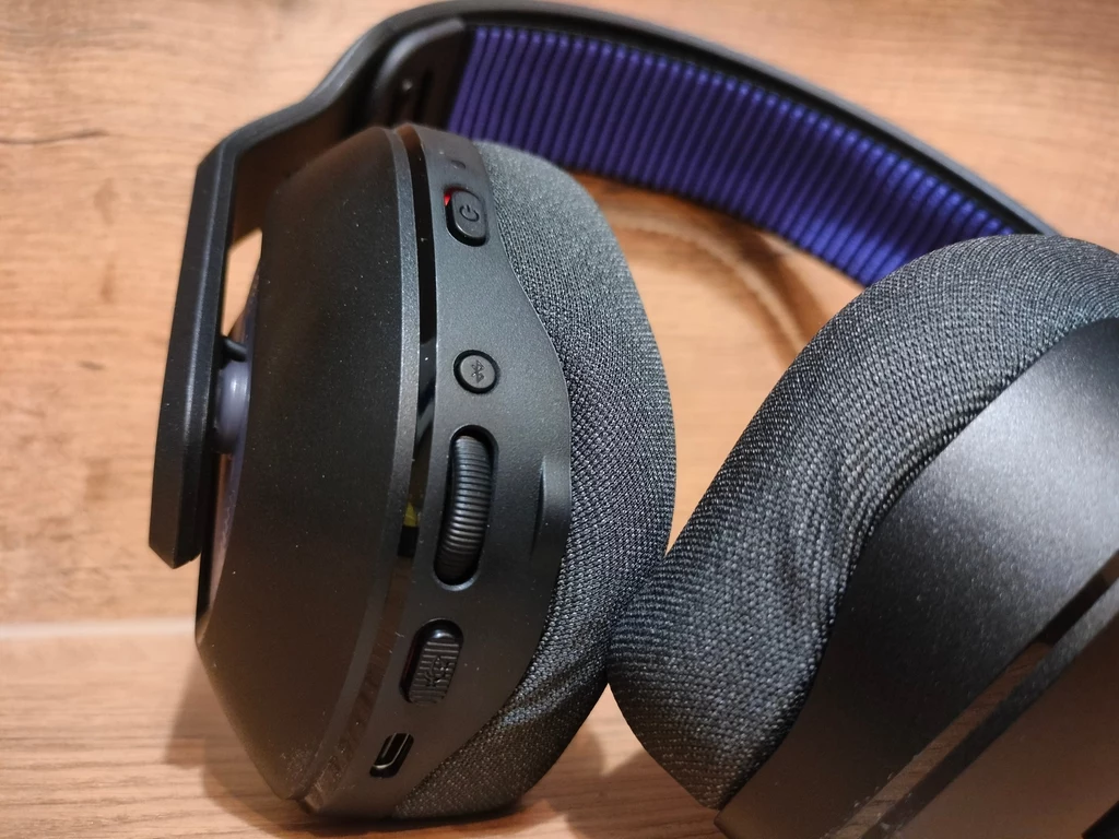 Logitech G522 Lightspeed Bezprzewodowe słuchawki nauszne z miękkimi poduszkami i widocznymi przyciskami sterującymi na jednej z muszli, wykończone elementami z tworzywa i metalowym pałąkiem z fioletową wyściółką.