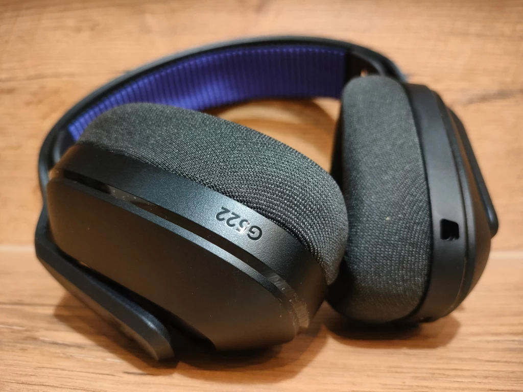 Logitech G522 Lightspeed Czarne, nauszne słuchawki z miękkimi poduszkami i oznaczeniem G332 na muszli, położone na drewnianej powierzchni, z widocznym niebieskim pałąkiem od wewnętrznej strony.