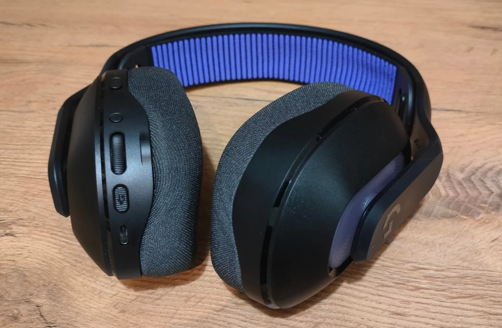 Logitech G522 Lightspeed Czarne słuchawki nauszne z wygodnymi, miękkimi nausznikami, pałąkiem z fioletowym paskiem i panelami z przyciskami funkcyjnymi, umieszczone na drewnianej powierzchni.