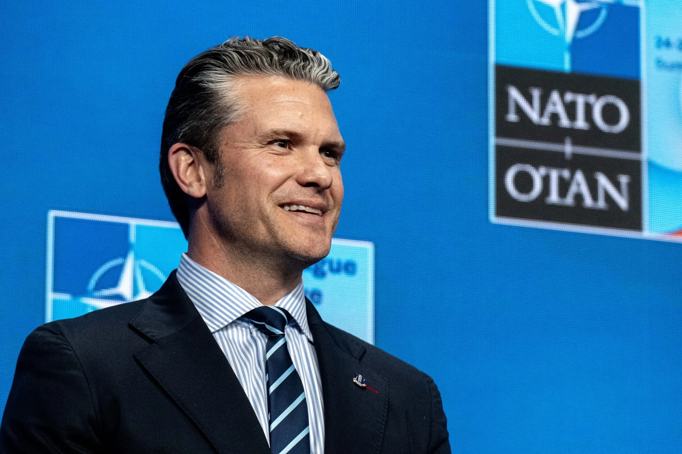 Pete Hegseth poinformował, że FBI wszczęło śledztwo w sprawie wycieku informacji o ataku na Iran Mężczyzna w garniturze z uśmiechem stoi na tle niebieskiej planszy z logo NATO, w tle widoczne anglo- i francuskojęzyczne oznaczenia sojuszu.
