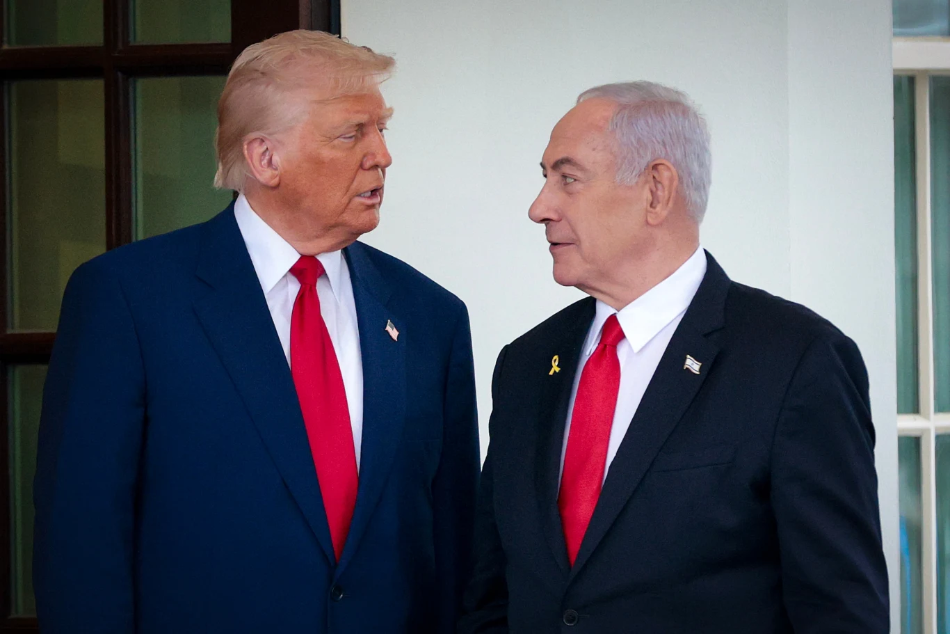 Donald Trump wychwala Binjamina Netanjahu. Twierdzi, że "USA go ocalą", zdj. z kwietnia 2025 roku Dwóch mężczyzn w garniturach, obaj mają przypięte flagi do klap marynarek oraz czerwone krawaty, stoją naprzeciw siebie i prowadzą rozmowę, w tle jasna ściana i drzwi.
