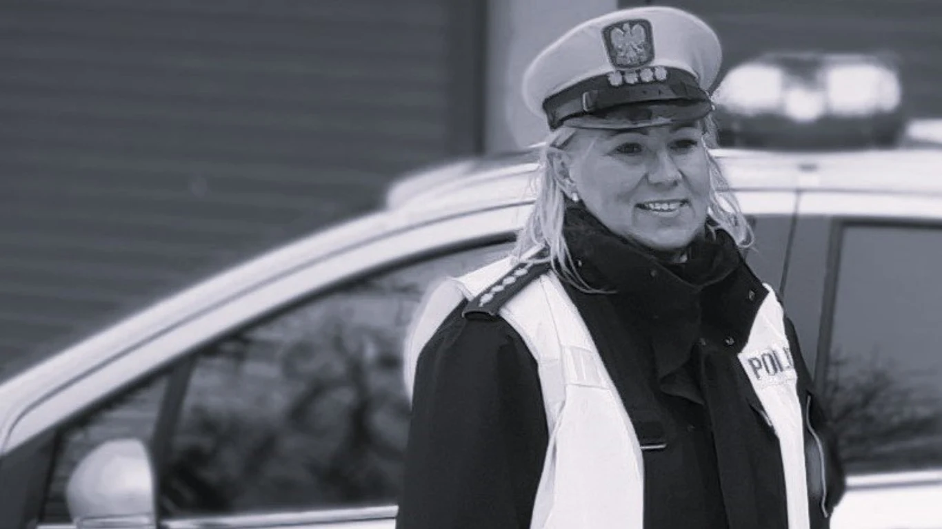 Nie żyje ceniona policjantka z Będzina. Iwona Bajan miała 49 lat Funkcjonariuszka policji w czapce z daszkiem i odblaskowej kamizelce stoi przed radiowozem, uśmiechając się, w tle widoczne rozmyte tło miejskie.