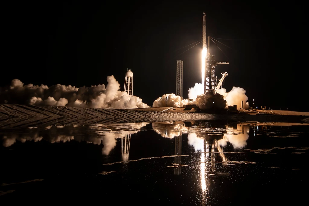 Start rakiety Falcon 9, która wyniosła Sławosza Uznańskiego-Wiśniewskiego w kosmos w środę z rana. Start rakiety kosmicznej nocą z intensywnym płomieniem i dymem unoszącymi się wokół wyrzutni, odbicie światła w wodzie potęguje efekt wizualny, otoczenie spowite ciemnością