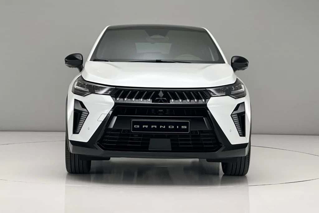 Białe auto typu SUV widoczne od frontu w studiu na białym tle, wyraźne reflektory, charakterystyczny grill i tablica rejestracyjna z napisem Grandis