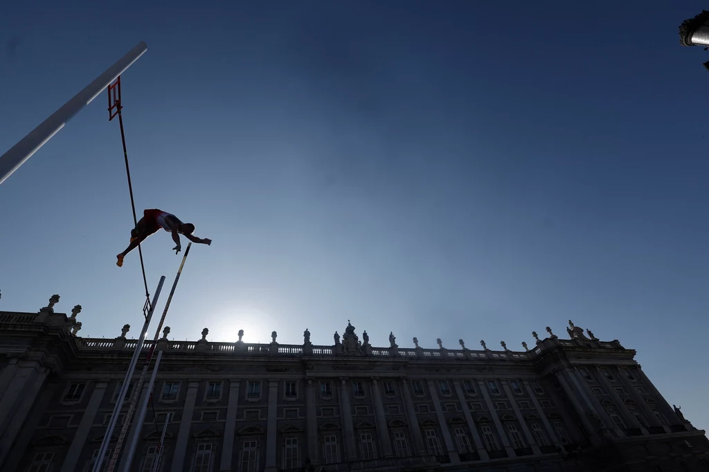 Piotr Lisek na Plaza de Oriente w Madrycie zapewnił Polsce 15 punktów Zawodnik wykonuje skok o tyczce na tle monumentalnego budynku w pełnym słońcu, sylwetka sportowca widoczna w dynamicznej pozie na tle nieba.