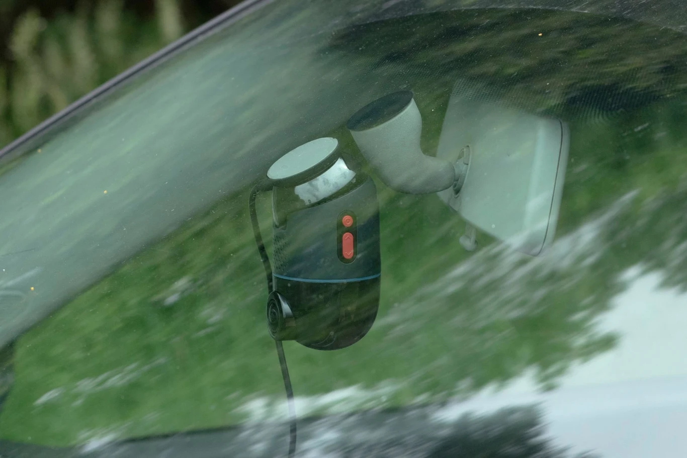 Kamera samochodowa zamocowana przy przedniej szybie pojazdu, widoczny uchwyt oraz przewód zasilający, lekkie odbicia otoczenia na szybie.