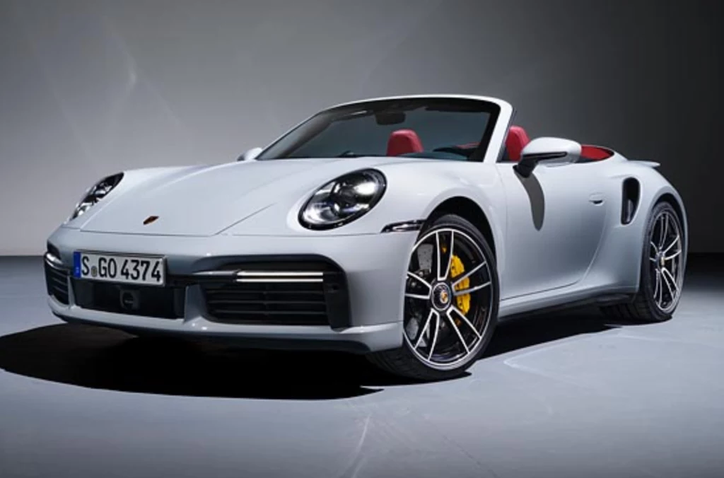 Najdroższy pojazd w Sejmie to Porsche 911 S Cabrio. Biały kabriolet Porsche stoi w dobrze oświetlonym studiu, felgi aluminiowe z żółtymi zaciskami hamulców, czerwone wnętrze kontrastujące z kolorem nadwozia, samochód ustawiony pod kątem ukazującym jego dynamiczną sylwetkę.