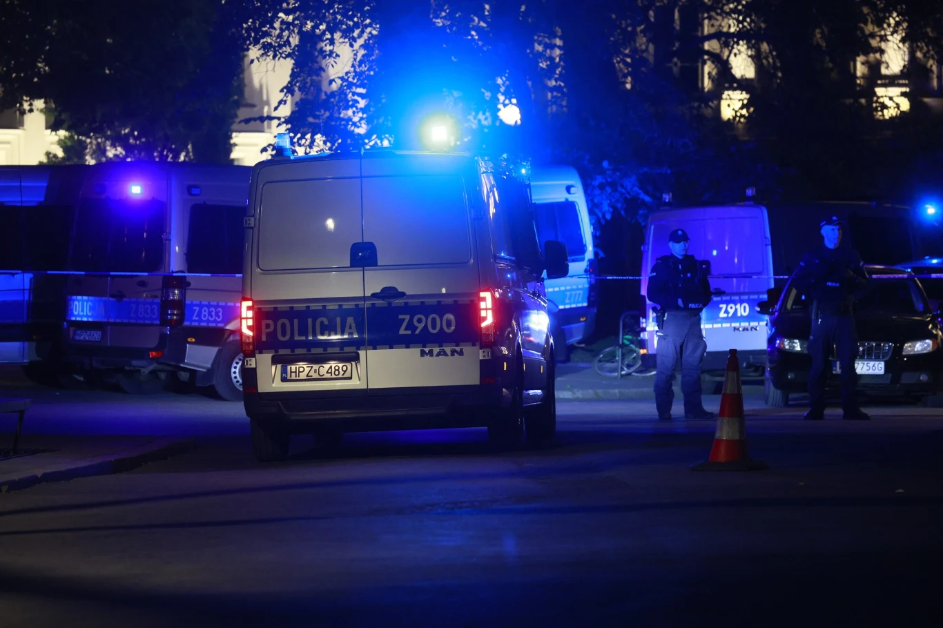 Zabójstwo na Uniwersytecie Warszawskim. Kolejne zarzuty dla Mieszka R. Funkcjonariusze policji i policyjne radiowozy z włączonymi światłami sygnalizacyjnymi podczas nocnej interwencji na ulicy, w tle widoczny policyjny bus oraz inne radiowozy, scena oświetlona niebieskim światłem.