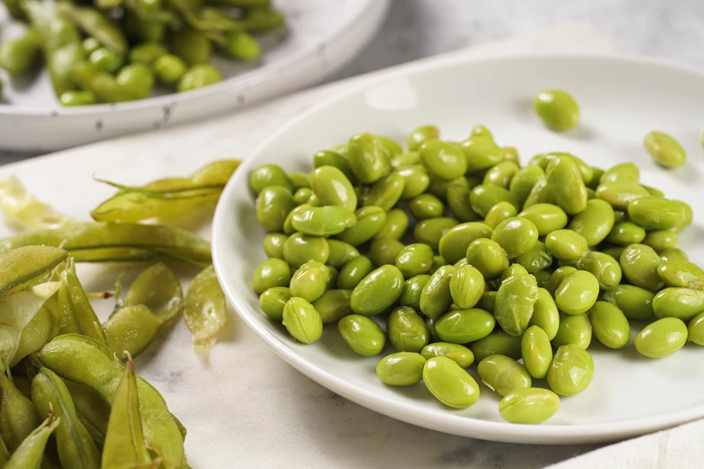 Edamame wygląda trochę jak bób. W Polsce można je kupić mrożone np. podczas tygodni azjatyckich w marketach Zielone ziarna edamame ułożone na białym talerzu, obok częściowo widoczne strąki po wyłuskaniu.