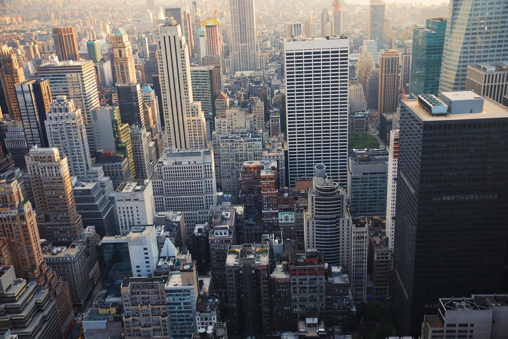 Widok na wieżowce Manhattanu w Nowym Jorku Gęsta zabudowa z wysokimi drapaczami chmur, wielkie biurowce tworzące charakterystyczną panoramę miasta z dominującymi prostokątnymi kształtami i licznymi oknami, w tle widoczna lekka mgiełka.