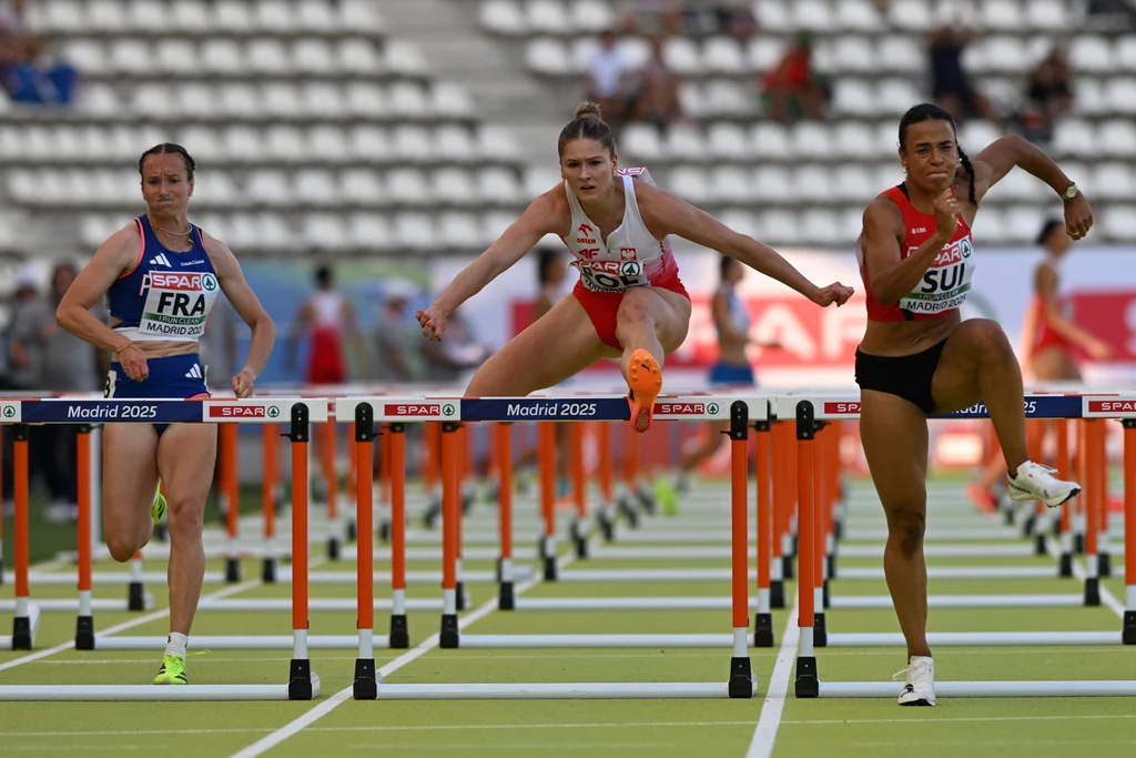 Ditaji Kambundji (z prawej) tym razem dużo lepsza od Pii Skrzyszowskiej Trzy kobiety uczestniczące w biegu przez płotki rywalizują na stadionie lekkoatletycznym, w tle widoczne puste trybuny