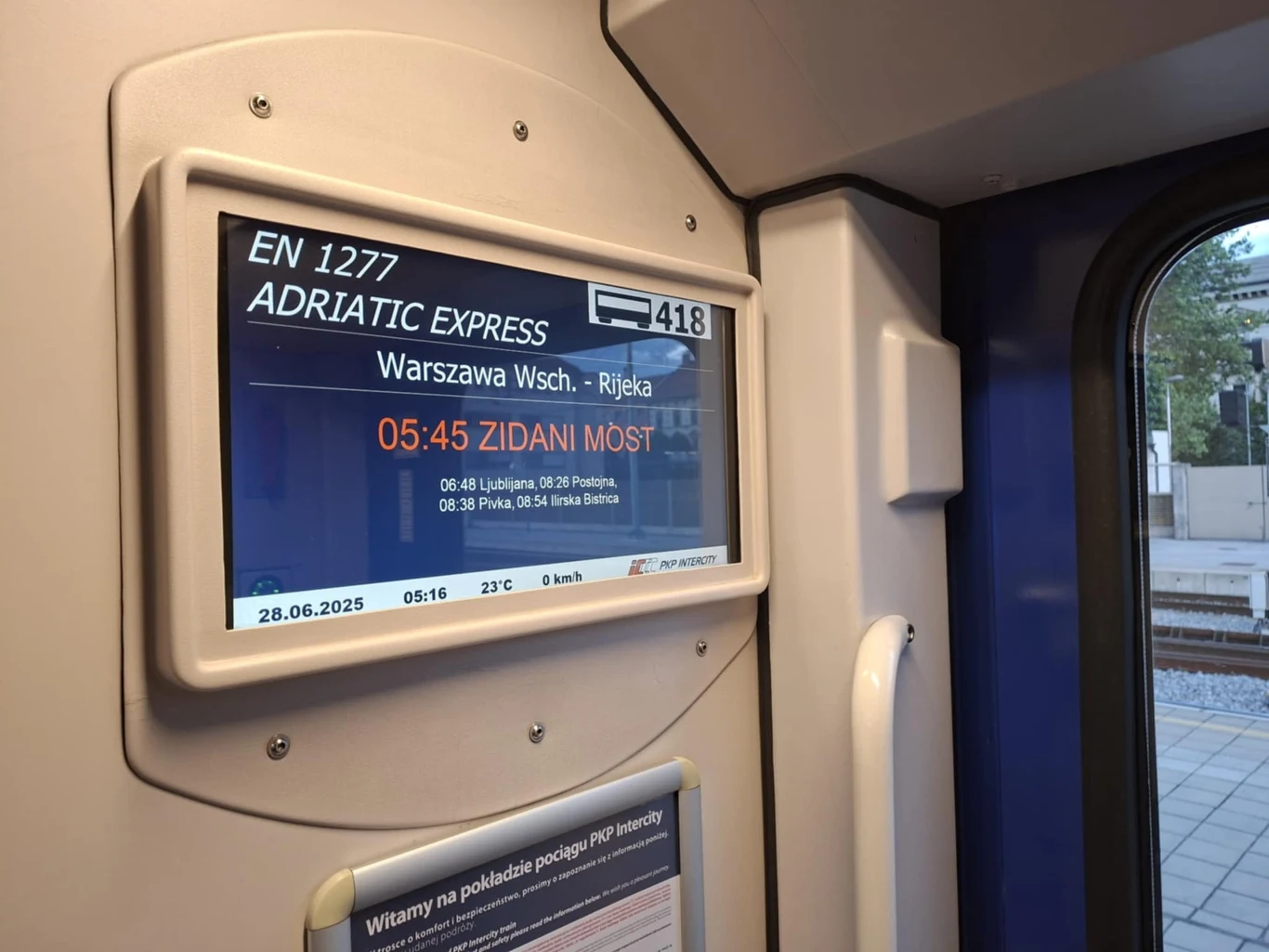 Elektroniczny wyświetlacz wewnątrz pociągu pokazujący szczegóły trasy Adriatic Express z Warszawy Wschodniej do Rijeki, z wyszczególnionymi godzinami i przystankami pośrednimi, datą oraz aktualną temperaturą powietrza.