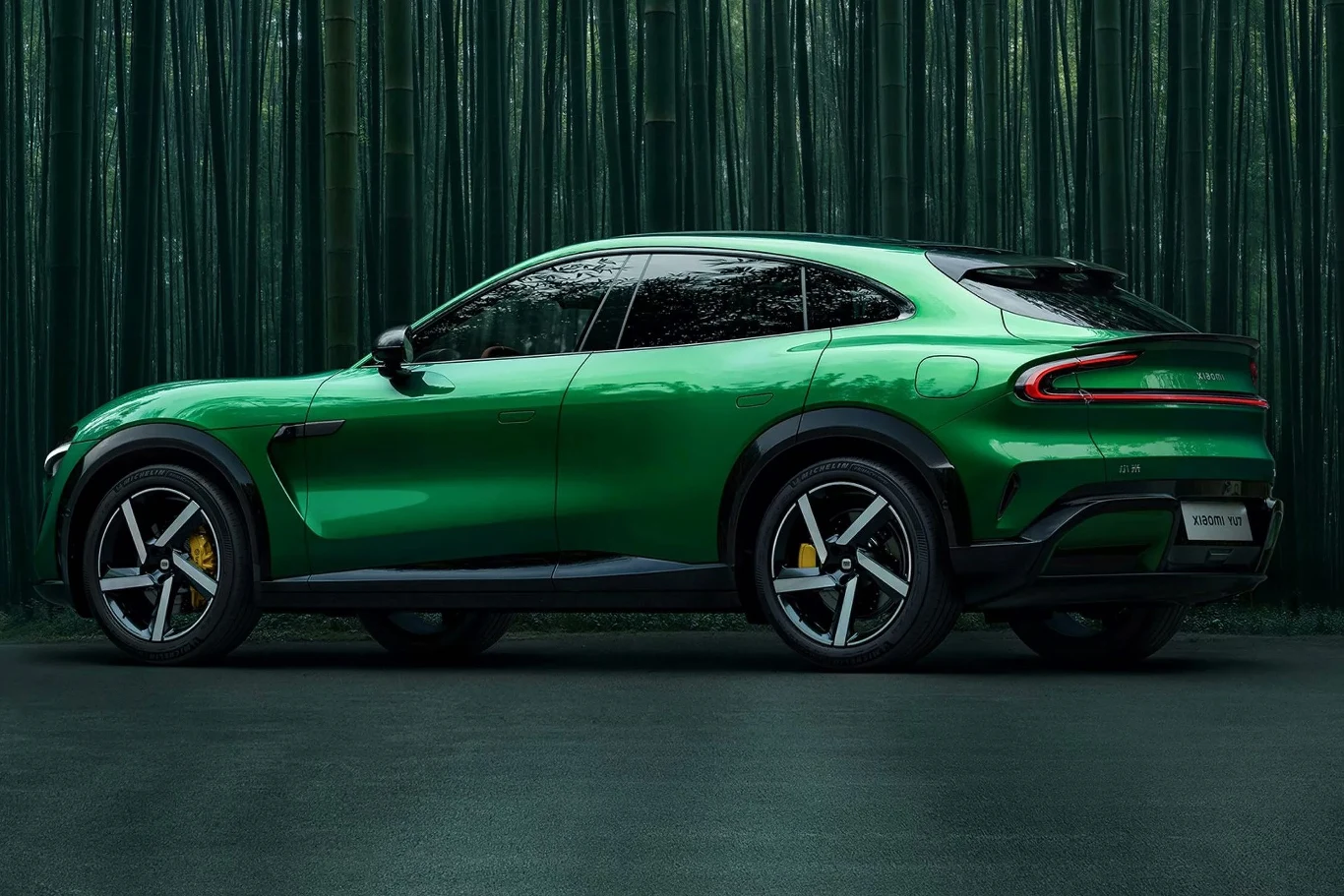 Zielony samochód typu SUV z czarnymi detalami i żółtymi zaciskami hamulcowymi stoi na tle gęstego lasu bambusowego, podkreślając nowoczesne linie nadwozia i sportowy charakter pojazdu.