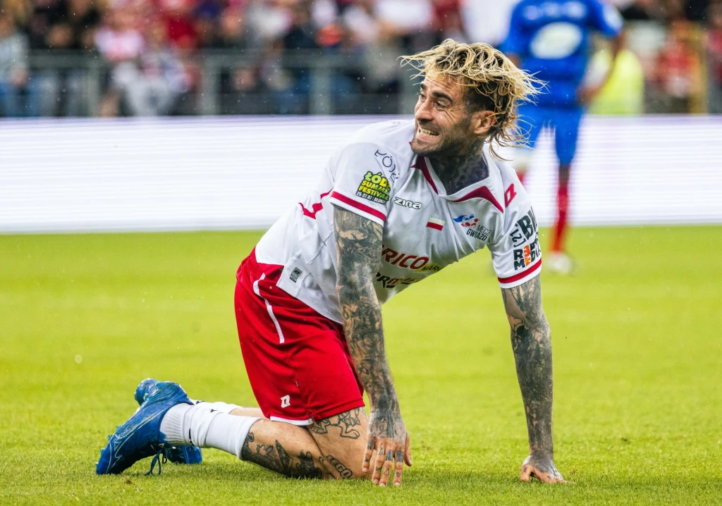 Quebonafide od jakiegoś czasu spełnia się także w roli piłkarza Piłkarz w stroju meczowym klęczy na murawie z wyrazem determinacji na twarzy, widoczne liczne tatuaże, za nim rozmyte postacie zawodników, tło stanowi stadion pełen kibiców.