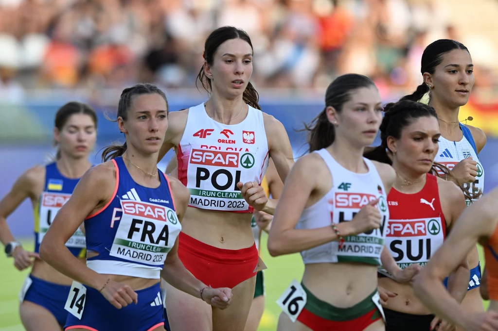 Kinga Królik Grupa lekkoatletek biegnących w trakcie zawodów na stadionie, zawodniczki reprezentują różne kraje i mają widoczne numery startowe oraz stroje narodowe.