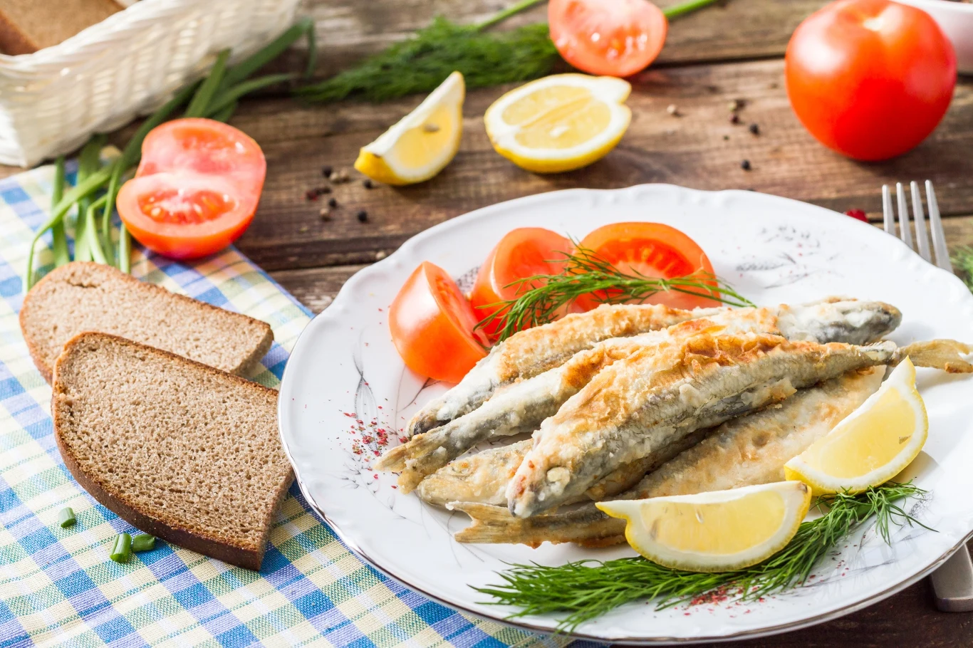 Smażone stynki to przysmak wielu mazurskich restauracji Talerz z usmażonymi rybami podanymi z plastrami cytryny, świeżym koperkiem oraz pomidorami, na obrusie leżą dwa kawałki chleba razowego, wokół talerza widoczne są składniki takie jak plasterki pomidora i cytryny.