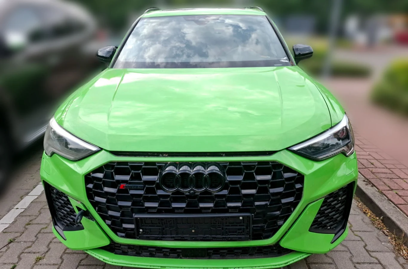 Audi RS Q3 z 2020 roku zostało odnalezione w Warszawie przez Służby Graniczne. Jaskrawozielone auto marki Audi zaparkowane na ulicy, sfotografowane od przodu. Charakterystyczny duży grill z logo oraz sportowy design samochodu wyróżniają pojazd na tle rozmytego, miejskiego otoczenia.