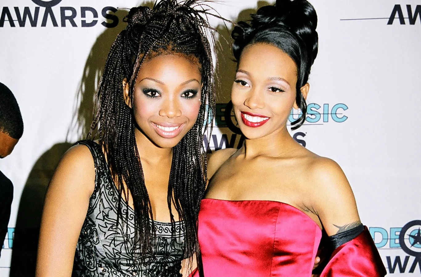 Brandy i Monica w 1998 r. Dwie uśmiechnięte kobiety pozujące razem na tle ścianki z logotypami imprezy, jedna ubrana w czarną sukienkę z koronką, druga w czerwoną suknię bez ramiączek, elegancko uczesane i starannie umalowane.