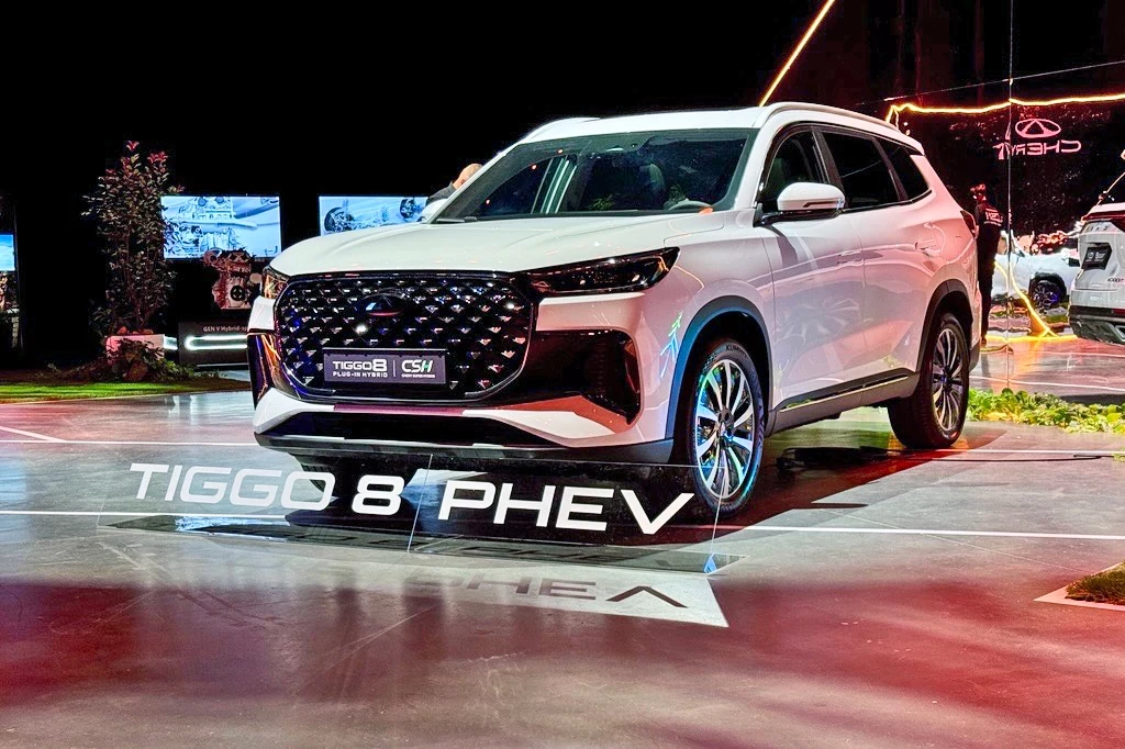 Chery Tiggo 8 Nowoczesny biały SUV Tiggo 8 PHEV prezentowany na podświetlonym stanowisku ekspozycyjnym, otoczony reflektorami i kolorowymi światłami, z wyraźnie widoczną nazwą modelu na podłodze.
