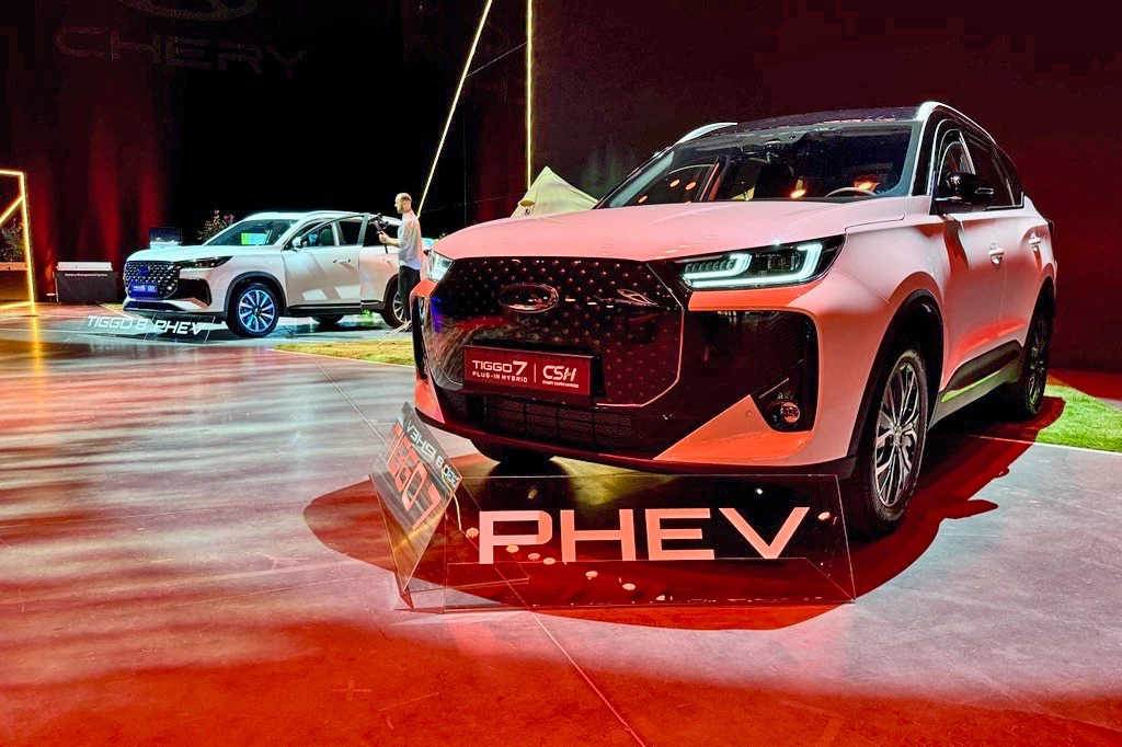 Chery Tiggo 7 oraz Chery Tiggo 8 Dwa nowoczesne SUV-y marki Chery, modele Tiggo 7 i CS1, eksponowane w jasnym oświetleniu na tle ciemnej hali wystawowej, podkreślone napisem PHEV oraz informacjami o wersji hybrydowej plug-in