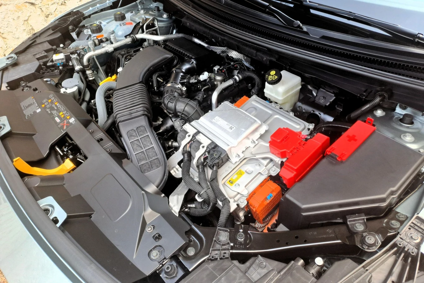 Silnik samochodu hybrydowego z widocznymi elementami układu elektrycznego, akumulatorami oraz przewodami, ułożonymi w uporządkowany sposób pod maską pojazdu.