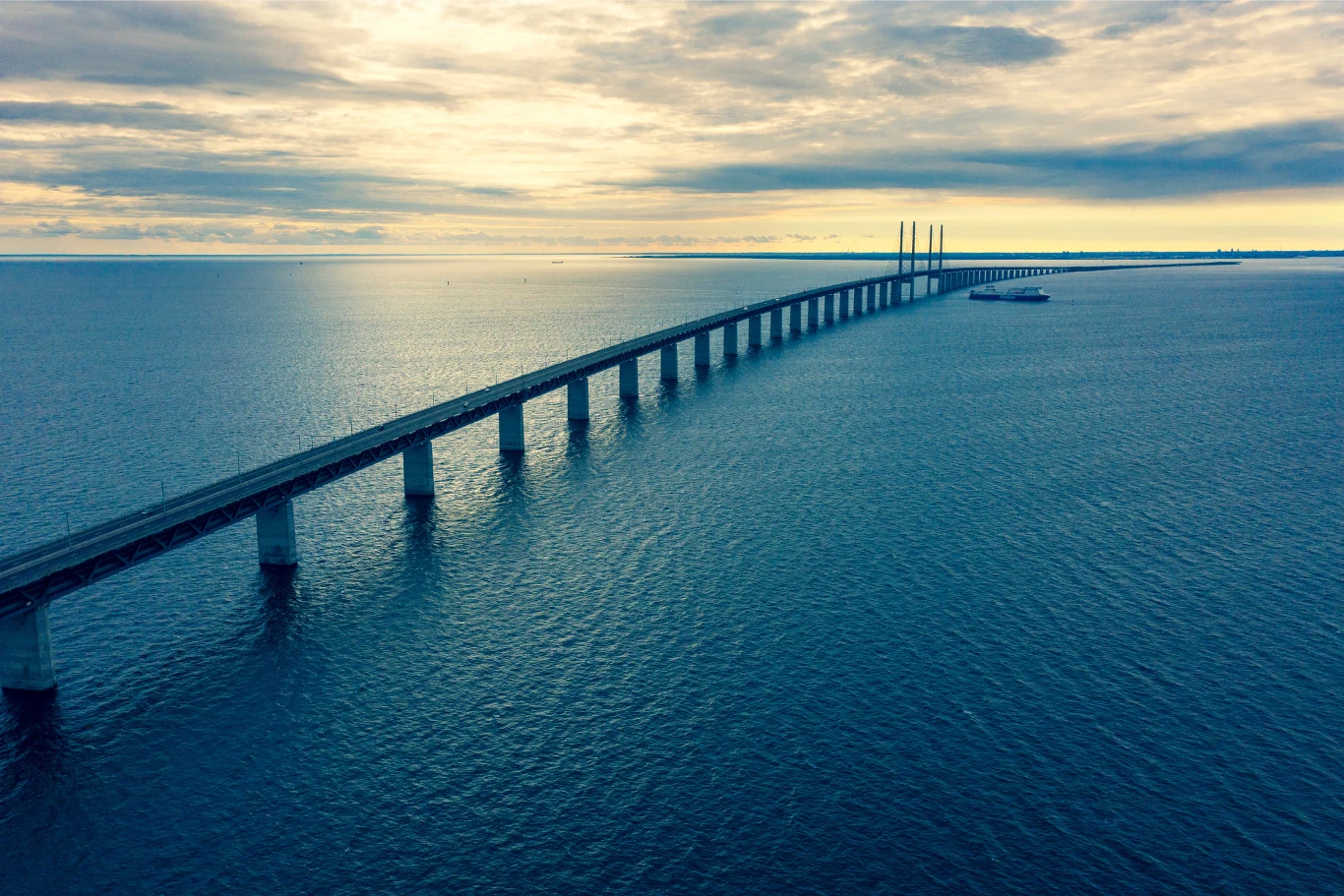 Most nad Sundem ma długość 7845 m. Długi most rozciągający się nad rozległą taflą wody, prowadzący w kierunku horyzontu pod zachmurzonym niebem.