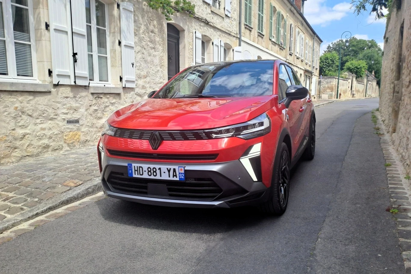 Czerwony samochód osobowy marki Opel Mokka zaparkowany na wąskiej ulicy wśród kamienic z jasnego kamienia, w tle zabudowa z oknami i zielenią.