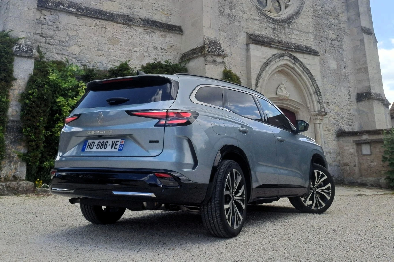 Srebrny SUV marki Renault Megane E-Tech zaparkowany przed kamiennym budynkiem o gotyckiej fasadzie z okrągłym oknem i rzeźbionym portalem.