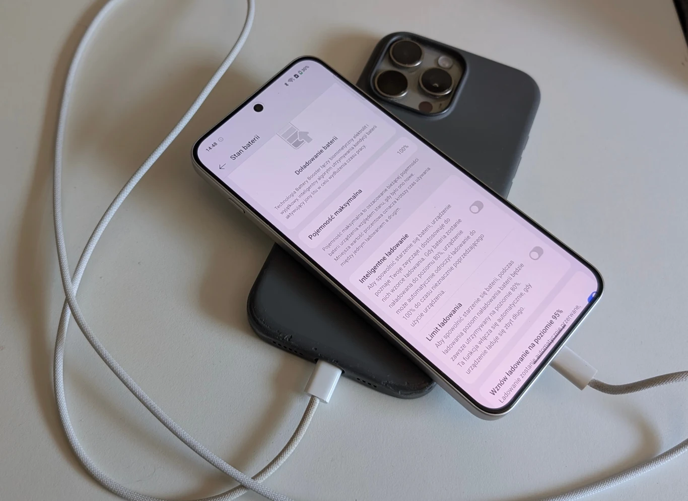OnePlus Nord 5 wspiera zwrotne ładowanie. Dwa nowoczesne smartfony leżące na białej powierzchni, jeden z nich podłączony do ładowania kablem USB-C, na ekranie widoczne są ustawienia systemowe.