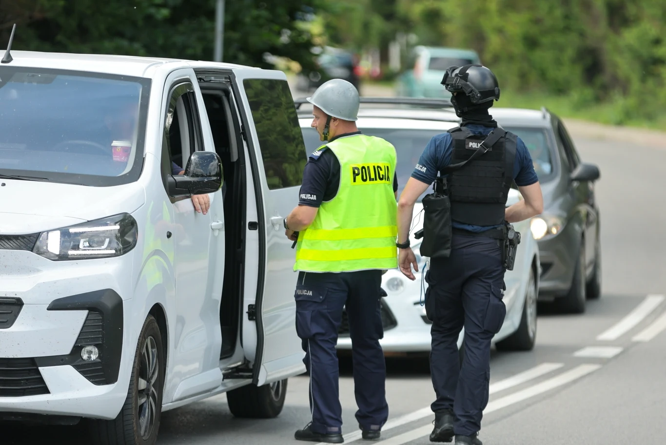 Nowy komunikat policji ws. poszuzkiwań Tadeusza Dudy Dwóch policjantów w kamizelkach i hełmie przeprowadza kontrolę kierowcy białego samochodu dostawczego na wiejskiej drodze, za pojazdem stoją kolejne auta.