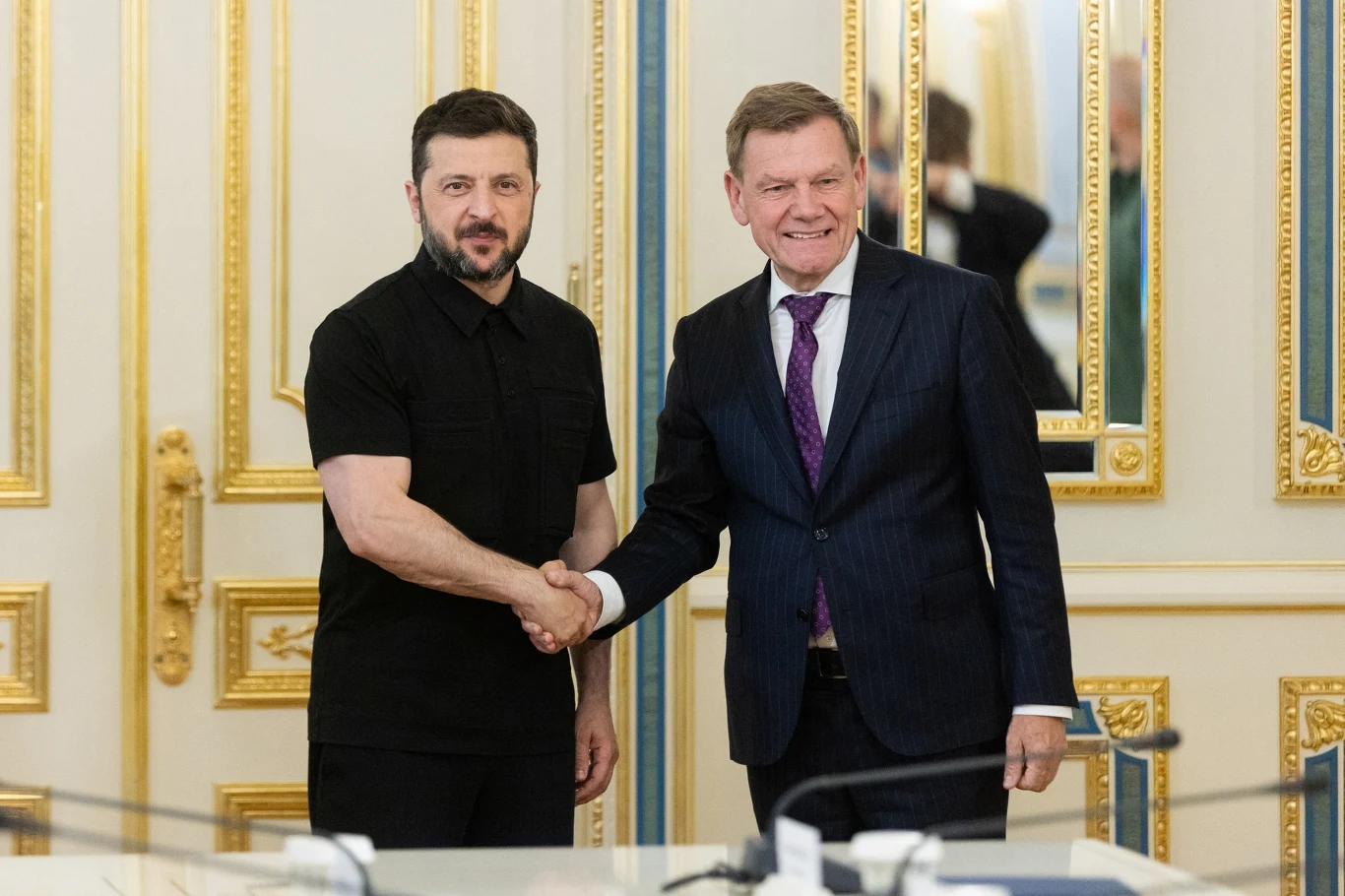 Prezydent Ukrainy Wołodymyr Zełenski i szef niemieckiej dyplomacji Johann Wadephul Dwóch mężczyzn podaje sobie ręce w eleganckim, bogato zdobionym wnętrzu, obaj uśmiechnięci, ubrani formalnie, w tle widać złote zdobienia na ścianach i drzwiach.