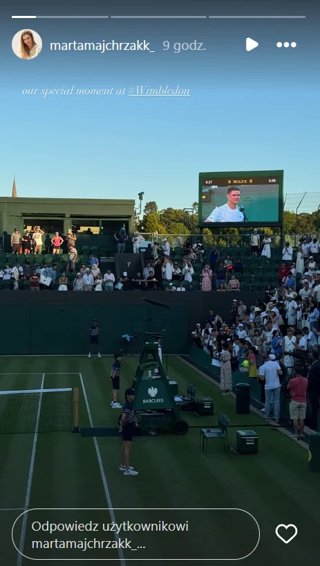 Marta Majchrzak podzieliła się wrażeniami po wygranej męża na Wimbledonie Kort tenisowy podczas turnieju, liczne osoby zgromadzone przy linii bocznej i na trybunach, na telebimie transmisja zbliżenia uczestnika lub uczestniczki meczu, po lewej części kadru widoczni sędziowie i obsługa.