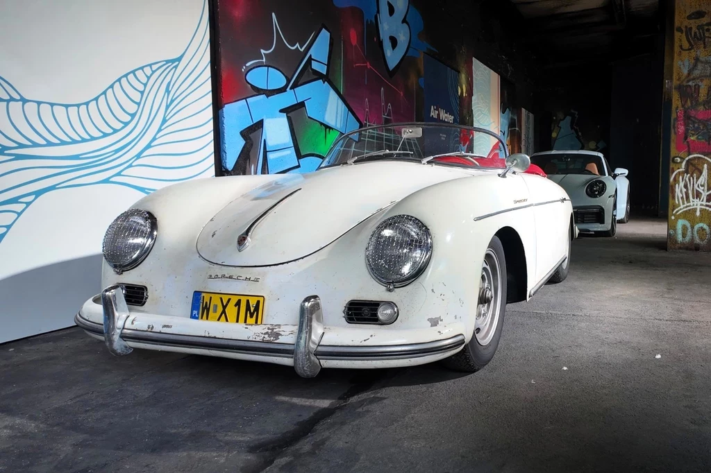 Również prywatni właściciele przygotowali sporo ciekawych samochodów. Wśród nich znalazło się m.in. kilka egzemplarzy Porsche 356 Speedster. Klasyczny biały samochód sportowy z widocznymi śladami zużycia stoi na tle muralu i graffiti w ciemnej, industrialnej przestrzeni, a w tle widać kolejny samochód.