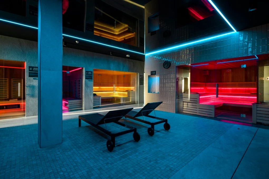 Hotel Crystal Mountain Wnętrze nowoczesnego centrum spa z podświetlanymi kabinami sauny w różnych kolorach, dwiema leżankami oraz eleganckim wystrojem i elementami neonowego oświetlenia.