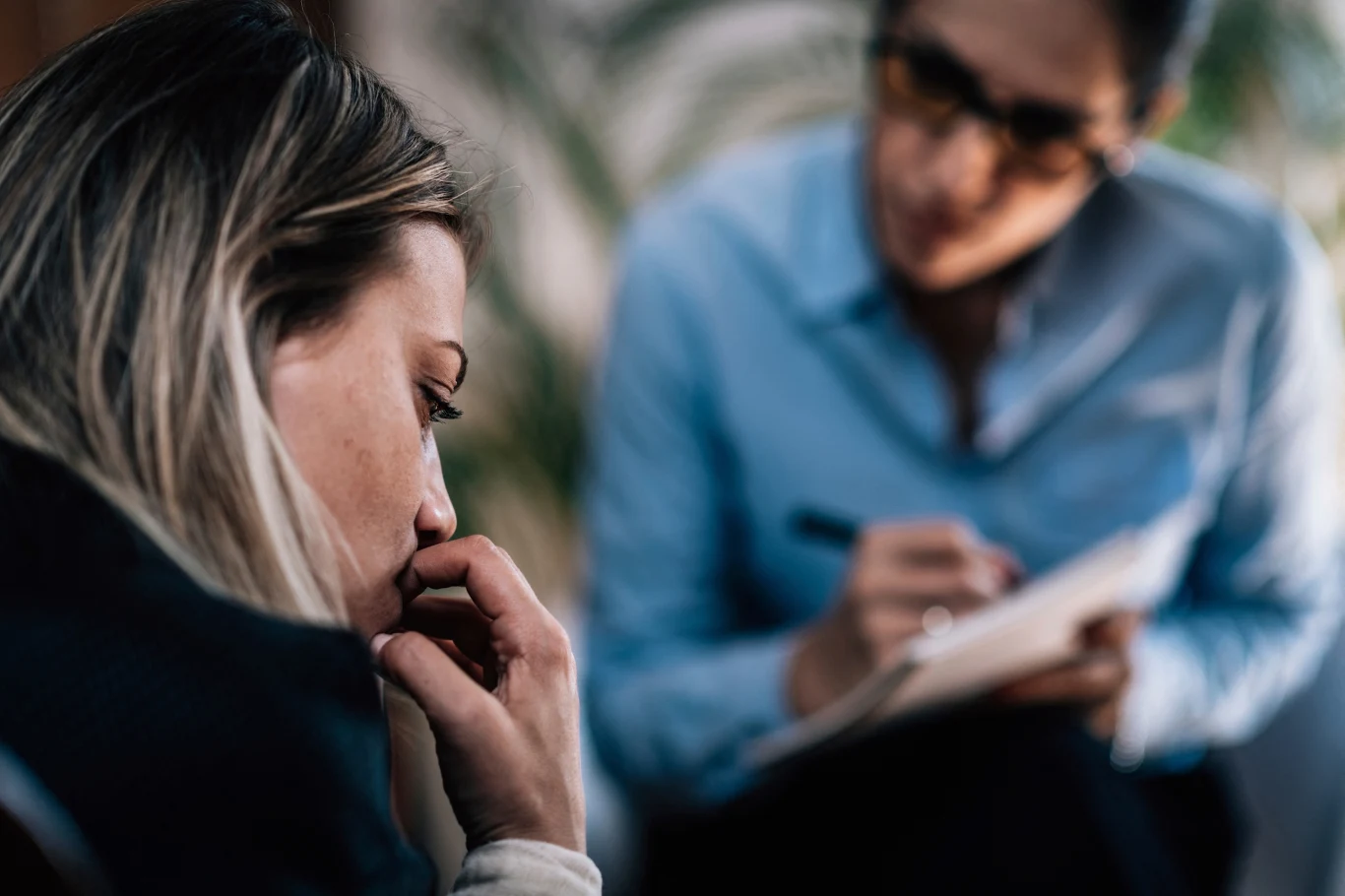 Gdy samodzielnie nie jesteśmy w stanie poradzić sobie z niepokojem, warto udać się do terapeuty Kobieta w zamyśleniu opiera głowę na ręku, a druga osoba z notatnikiem i długopisem uważnie słucha, zapisując informacje.
