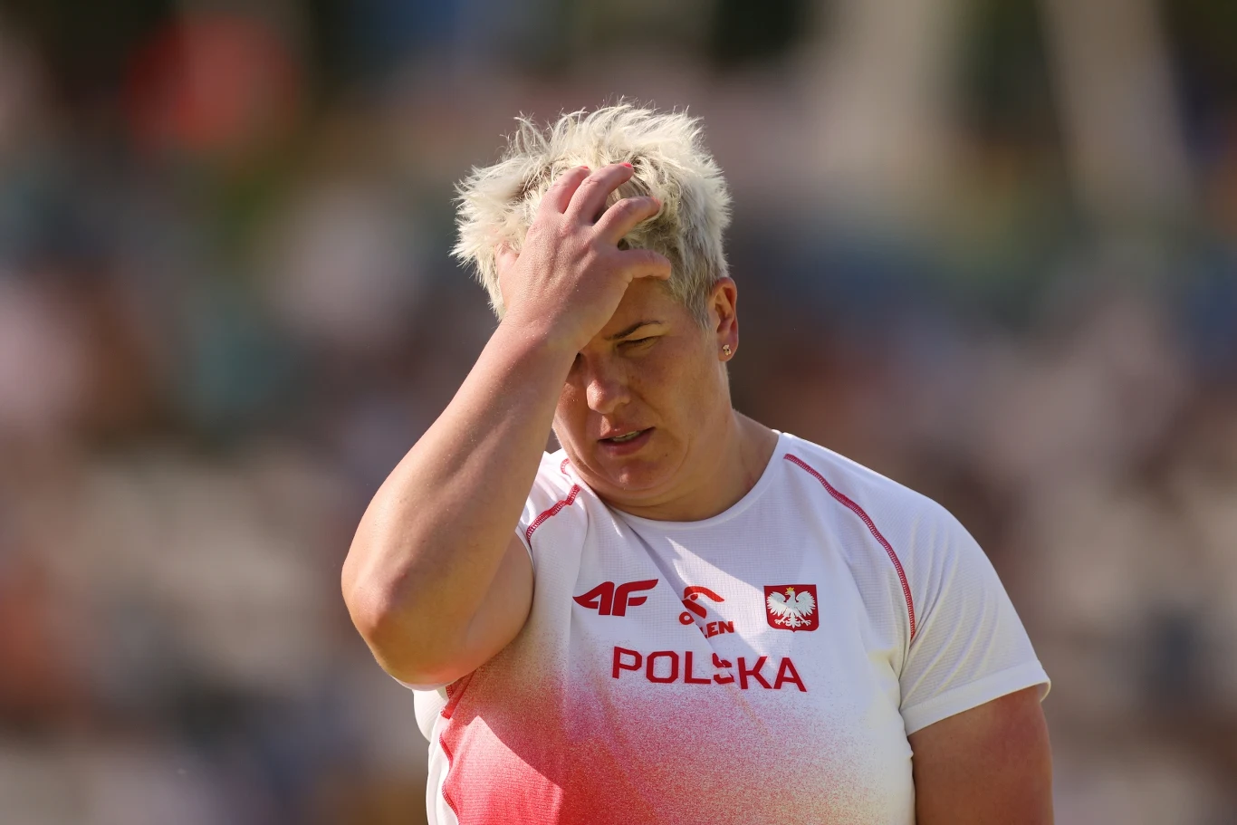 Anita Włodarczyk w sobotę triumfowała w Madrycie. A już za kilka dni ma rzucać na słynnym Hayward Field w Eugene Zawodniczka w białej koszulce z napisem 'Polska' i polską flagą, trzymająca się za głowę z wyrazem zmartwienia lub frustracji, na tle rozmazanego stadionu sportowego.
