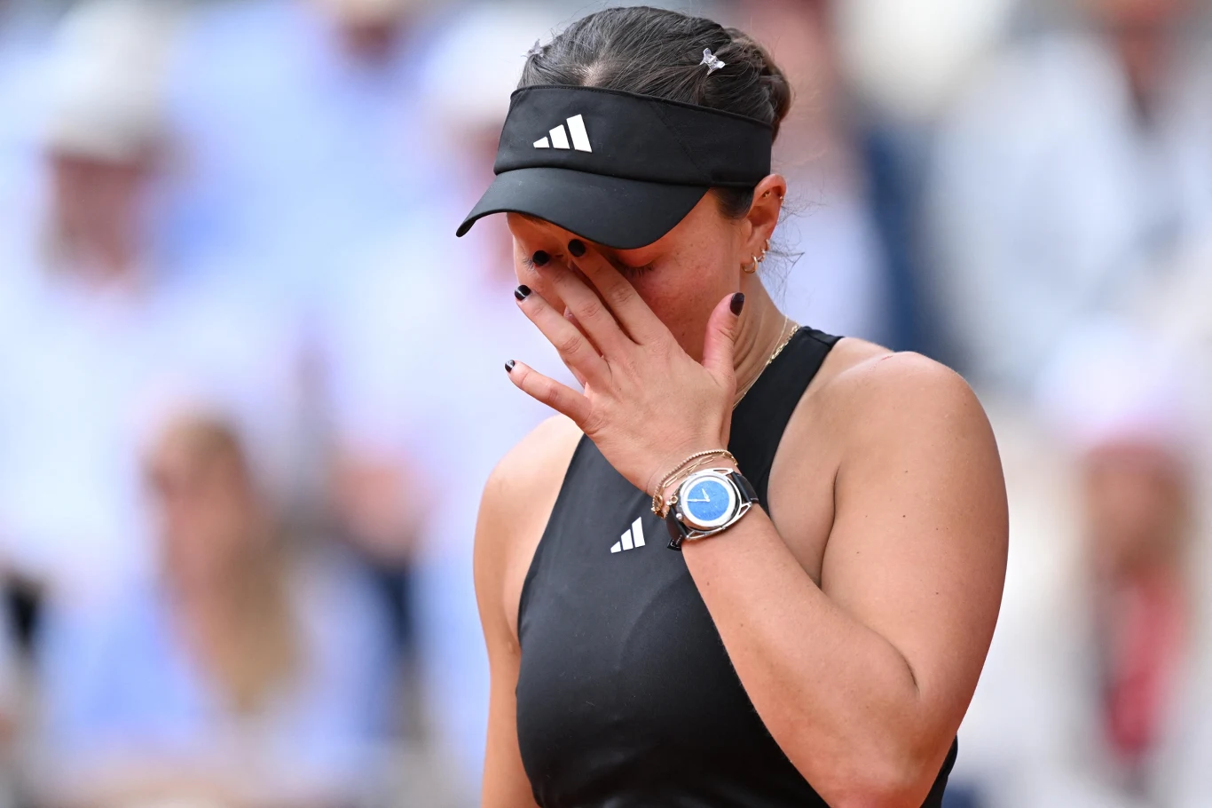 Zawodniczka tenisowa w sportowym stroju i czapce z daszkiem, z ręką na twarzy w geście emocji, na tle rozmytej publiczności.