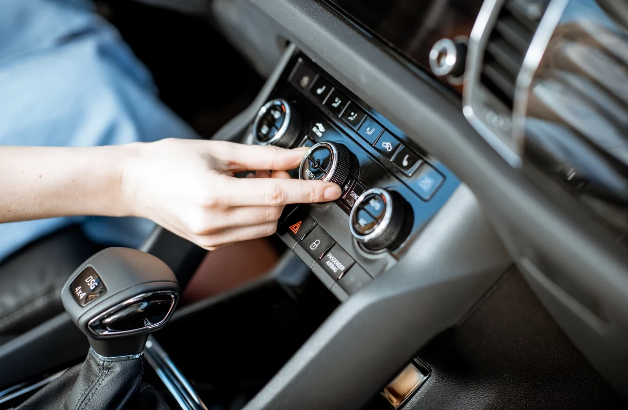 Jak szybko schłodzić auto w upał? Ręka osoby regulująca pokrętło klimatyzacji w nowoczesnym wnętrzu samochodu, widoczna dźwignia zmiany biegów oraz panel sterowania urządzeniami pokładowymi