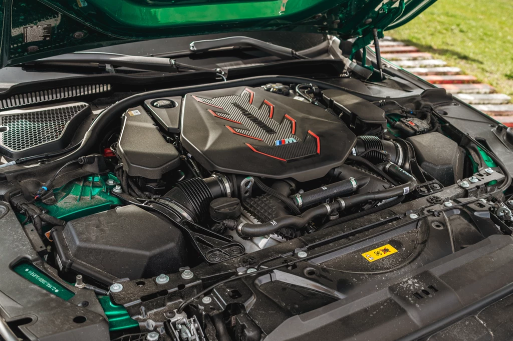 Nowe M5 jest hybrydą plug-in, ale pod maską nadal pracuje doładowane V8 Silnik samochodu sportowego z wyraźnym oznaczeniem M oraz charakterystycznymi czerwoną i niebieską linią na pokrywie, detale mechaniczne i nowoczesne elementy konstrukcyjne podkreślają wydajność oraz przeznaczenie pojazdu o wysokich osiągach.