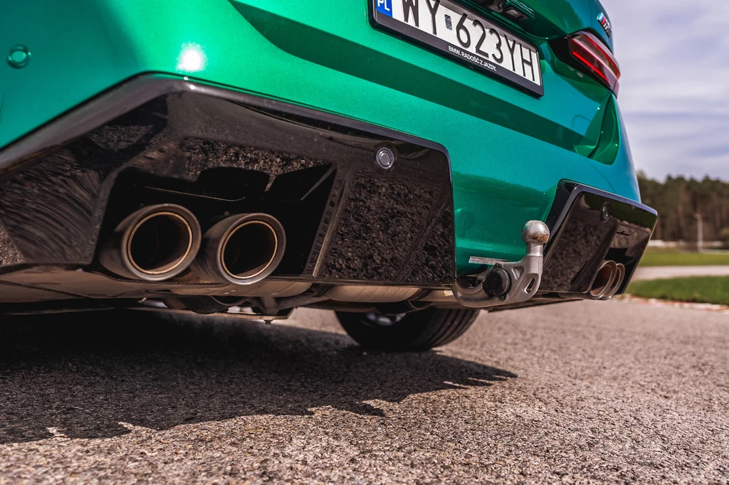 BMW M5 Touring pociągnie przyczepę o masie do 2000 kg Tył zielonego samochodu z widocznym podwójnym wydechem, hakiem holowniczym i fragmentem tablicy rejestracyjnej, sfotografowany na asfaltowej drodze.