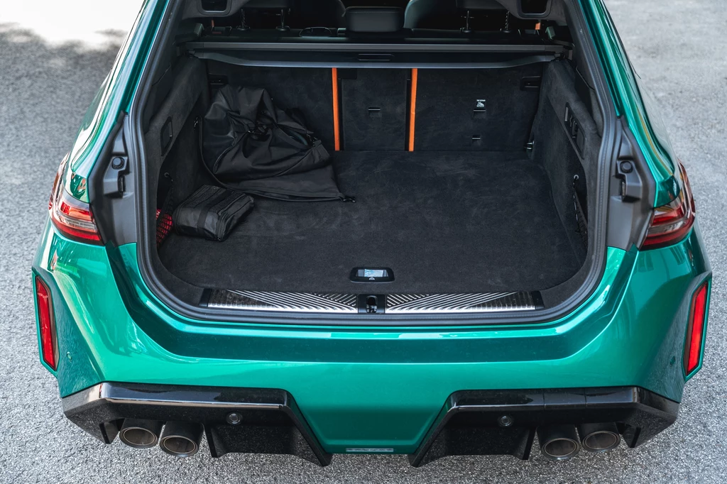 Bagażnik w M5 Touring ma tylko 500 l - o 70 l mniej niż w pozostałych wersjach serii 5. Również tych z napędem plug-in Otwarty bagażnik zielonego samochodu sportowego, pusta przestrzeń wyłożona czarną tapicerką, na lewej stronie widoczna złożona torba oraz niewielka paczka, tylne lampy o nowoczesnym kształcie.