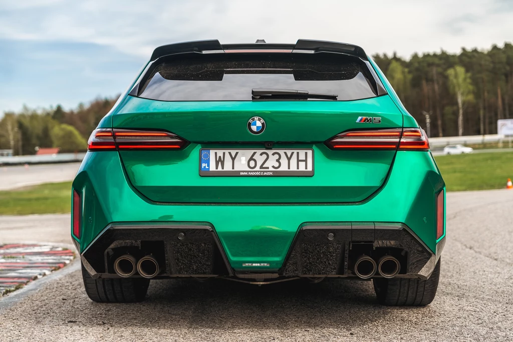 Cztery końcówki wydechu w M5 są nie tylko na pokaz - brzmienie (jak na współczesne seryjne auto) jest naprawdę niezłe Zielony samochód sportowy marki BMW M z polską rejestracją, ujęcie od tyłu, widoczne cztery końcówki wydechu, dynamiczna linia nadwozia oraz elementy aerodynamiczne, w tle asfaltowy tor i drzewa.