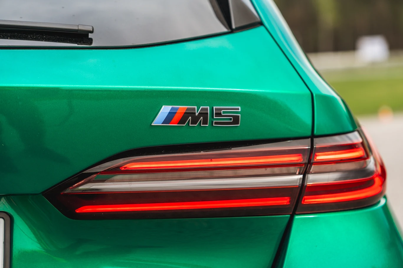 Tylna część zielonego samochodu BMW M5 z wyraźnie widocznym logo modelu oraz nowoczesnym światłem tylnym.