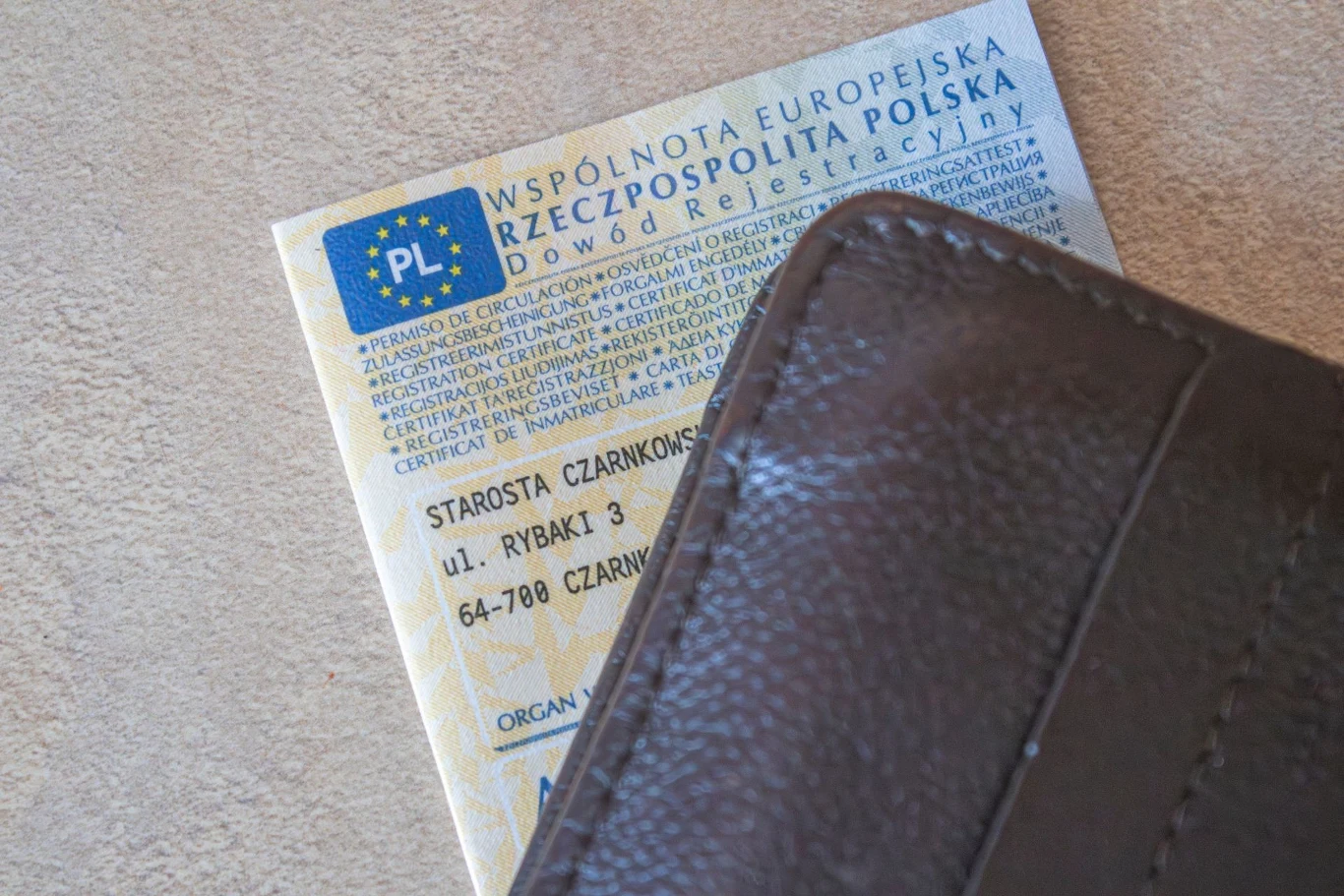Czy za brak dowodu rejestracyjnego grozi mandat? Dowód rejestracyjny pojazdu częściowo wystający z brązowego portfela, tekst i elementy graficzne dokumentu widoczne na górnej części