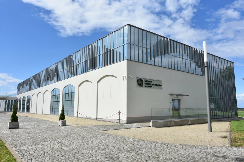 Nowoczesny budynek Muzeum Pierwszych Piastów został otwarty zaledwie trzy lata temu Nowoczesny budynek o przeszklonej elewacji, z nazwą Instytutu Pamięci Narodowej oraz Muzeum na ścianie frontowej, otoczony brukowanym placem, utrzymany w minimalistycznym stylu architektonicznym, z elementami zieleni przed wejściem.