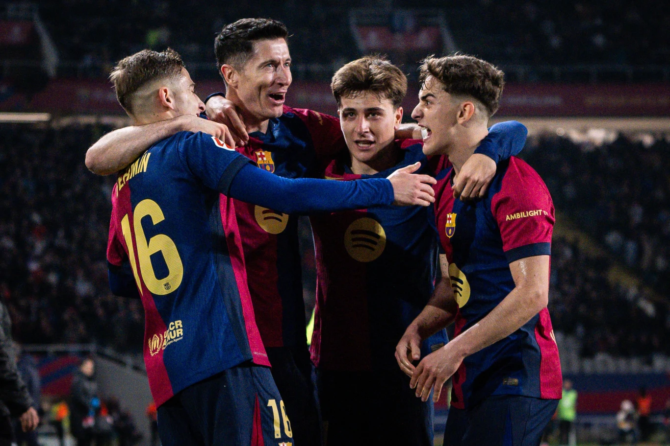 Kilku piłkarzy drużyny FC Barcelona w ciemnoczerwono-niebieskich strojach świętuje razem na murawie stadionu, obejmując się i uśmiechając.