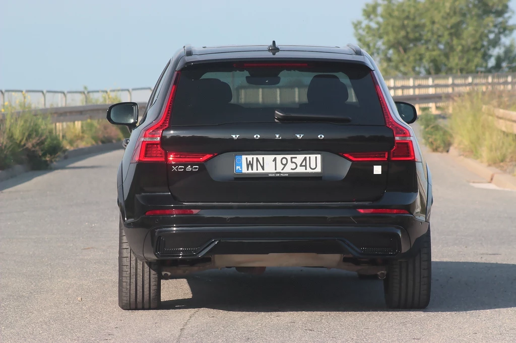 Jeśli kierowca Volvo XC60 eAWD zapragnie to niemal każdy będzie oglądał jego auto z tej perspektywy Czarny samochód marki Volvo XC 60 zaparkowany tyłem na opuszczonej drodze z wyraźnie widoczną rejestracją i charakterystycznymi tylnymi światłami.