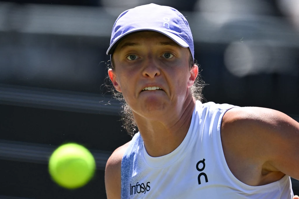 Iga Świątek rywalizowała z Poliną Kudiermietową w pierwszej rundzie Wimbledonu Kobieta w sportowym stroju i czapce skupiona na uderzeniu nadlatującej piłki tenisowej podczas meczu tenisowego.