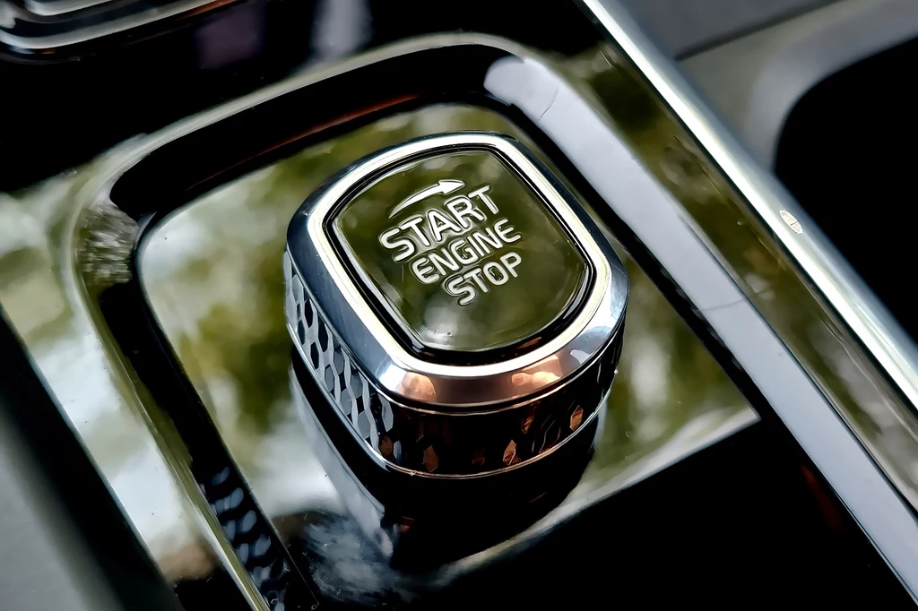 Volvo XC60 Srebrny przycisk z napisem START ENGINE STOP umieszczony na lśniącej konsoli samochodu, otoczony elementami chromowanymi i odbiciami otoczenia.